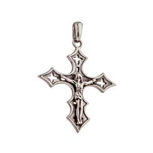 May include: A silver-coloured pendant in the shape of a cross. The cross features a detailed depiction of Jesus Christ and decorative cutouts. The pendant has a loop at the top for a chain.