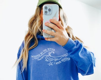 Puede incluir: Una sudadera con capucha azul real con un estampado gráfico blanco que dice "Washed by the Water I Have Decided" con una ola y una estrella de mar.