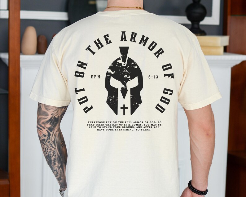 May include: A white t-shirt with a black graphic of a Spartan helmet and the text "Put on the Armor of God" with the scripture reference "Eph 6:13".