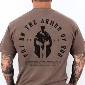 May include: A brown t-shirt with a black graphic of a helmet and the text "Put on the Armor of God" with the scripture reference "Eph 6:13".