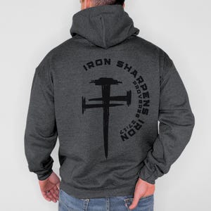 May include: Dark gray hoodie with a black graphic of a cross and the text "IRON SHARPENS IRON PROVERBS 27:17" in a semi-circle above the cross. The hoodie has a hood and long sleeves.