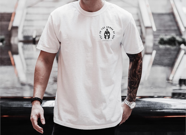 May include: White t-shirt with a black graphic of a helmet and the text "Put on the Armor of God Ephesians 6:11".