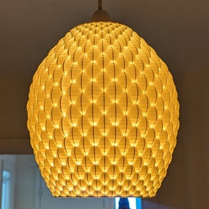 May include: A round, white, hanging light fixture with a geometric pattern. The light is on and emits a warm, yellow glow.