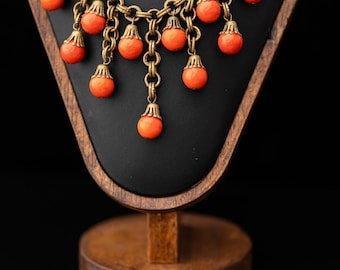 May include: A necklace and matching bracelet set featuring antique brass-toned metal chains adorned with dangling, round, bright orange beads. Each bead is capped with a decorative, scalloped metal finding, creating a layered, fringe-like effect.