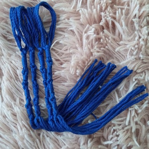 Peut inclure: Ensemble de cordons macramé bleu vif, noués et bouclés, disposés sur une surface rose clair douce et texturée. Les cordons sont soigneusement regroupés, avec plusieurs brins s'étendant des sections nouées.