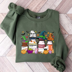 May include: Green sweatshirt with a Halloween-themed graphic featuring four bottles with witch hats and the words "Diprivan", "Fentanyl", "Ativan", and "Midazolam" printed on them.