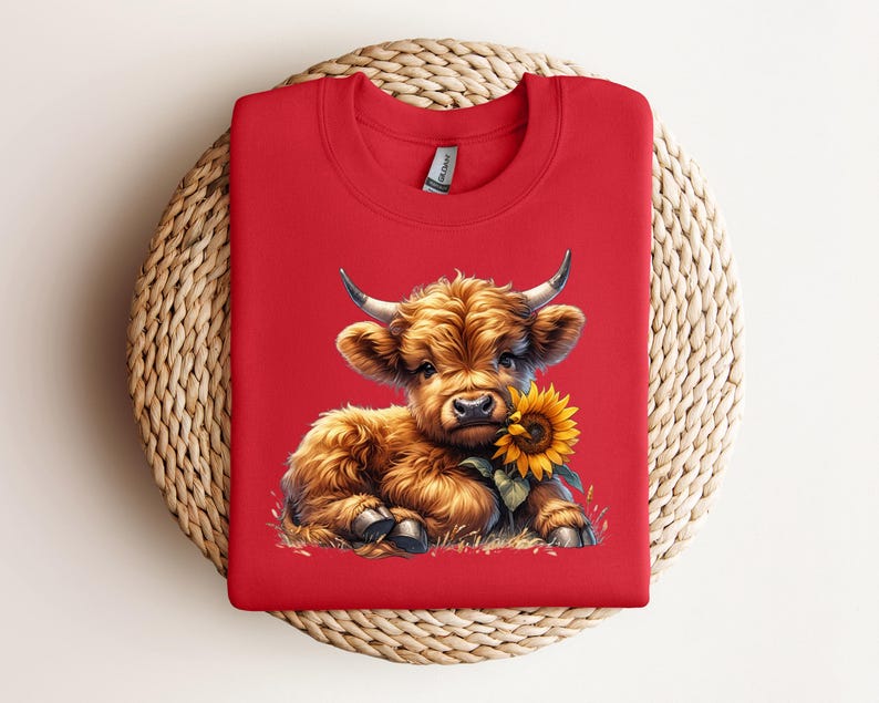 May include: Red t-shirt with a cartoon image of a brown Highland cow calf holding a yellow sunflower.