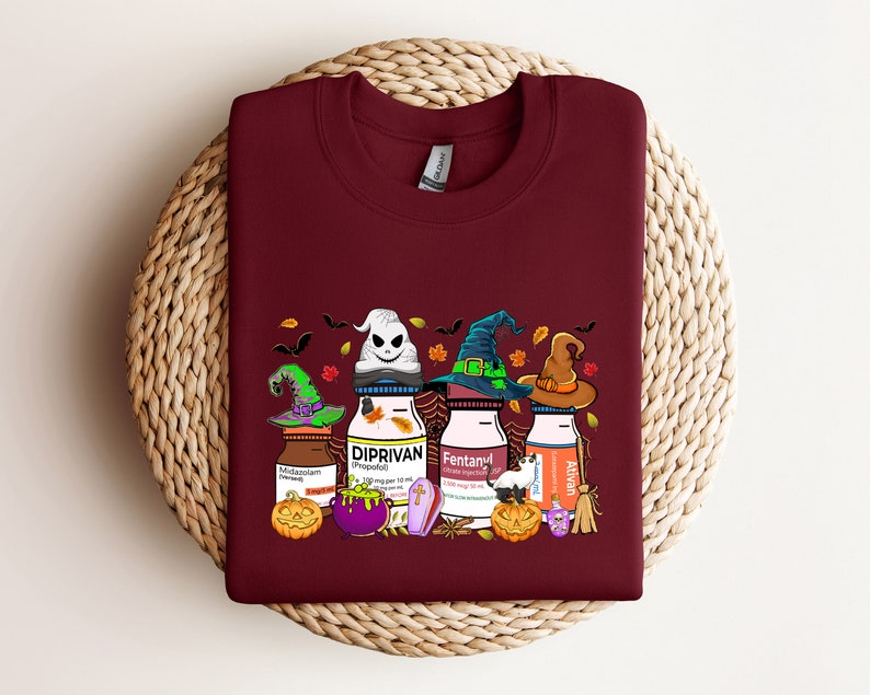 May include: A maroon t-shirt with a Halloween-themed design featuring three bottles with witch hats and the words "Diprivan", "Fentanyl", and "Ativan" on them.