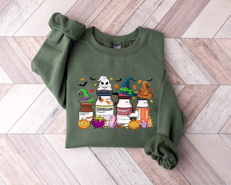 May include: Green sweatshirt with a Halloween-themed graphic featuring four bottles with witch hats and the words "Diprivan", "Fentanyl", "Ativan", and "Midazolam" printed on them.