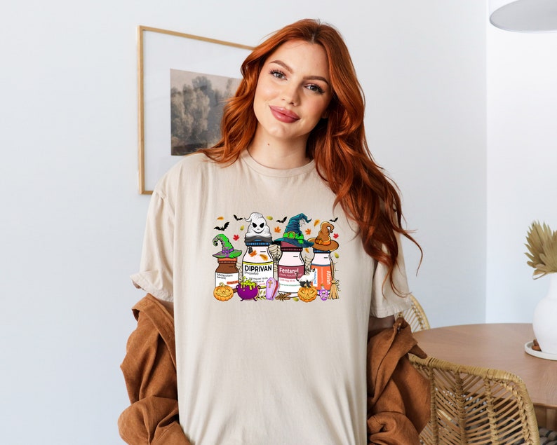 May include: A beige t-shirt with a Halloween-themed graphic featuring four bottles with witch hats and the text "Diprivan" and "Fentanyl".