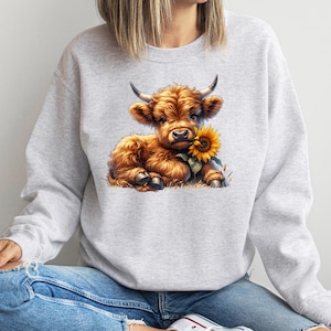 May include: A gray sweatshirt with a cute cartoon illustration of a brown Highland cow holding a yellow sunflower.