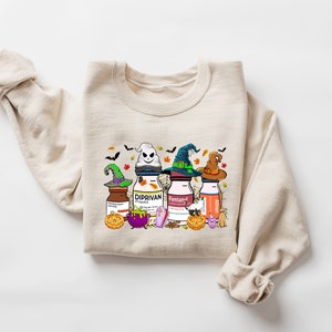 May include: A beige sweatshirt with a Halloween-themed graphic print featuring four bottles with witch hats and the words "Diprivan", "Fentanyl", and "Ativan".