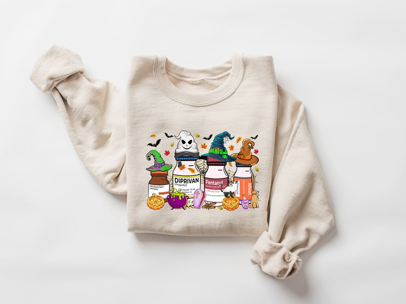 May include: A beige sweatshirt with a Halloween-themed graphic print featuring four bottles with witch hats and the words "Diprivan", "Fentanyl", and "Ativan".