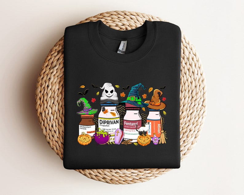 May include: Black t-shirt with a Halloween-themed graphic featuring three bottles of medication with witch hats and pumpkins. The bottles are labeled "Midazolam", "Diprivan", "Fentanyl", and "Alvan".