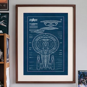 Puede incluir: Una lámina artística enmarcada con el plano técnico de la U.S.S. Enterprise de Star Trek, presentada en un marco de madera oscura con paspartú blanco. El diseño muestra dibujos técnicos de la nave en blanco sobre un fondo azul.
