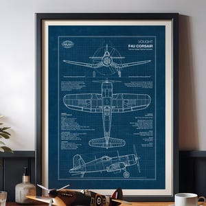 Puede incluir: Plano enmarcado de un avión de combate embarcado Vought F4U Corsair. El plano es blanco sobre fondo azul. Una maqueta del mismo avión se encuentra sobre una mesa de madera frente al plano enmarcado.