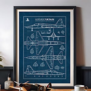 Może przedstawiać: Oprawiony wydruk z planem odrzutowca Northrop T-38 Talon. Wydruk przedstawia szczegółowe białe rysunki liniowe samolotu na ciemnoniebieskim tle kratki. Model samolotu stoi na drewnianej powierzchni.