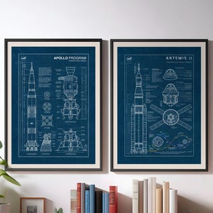 Puede incluir: Dos impresiones enmarcadas estilo plano. La impresión izquierda está etiquetada como "Apollo Program" y la derecha como "Artemis II". Ambas impresiones presentan dibujos técnicos detallados de cohetes y naves espaciales en blanco sobre un fondo azul oscuro.