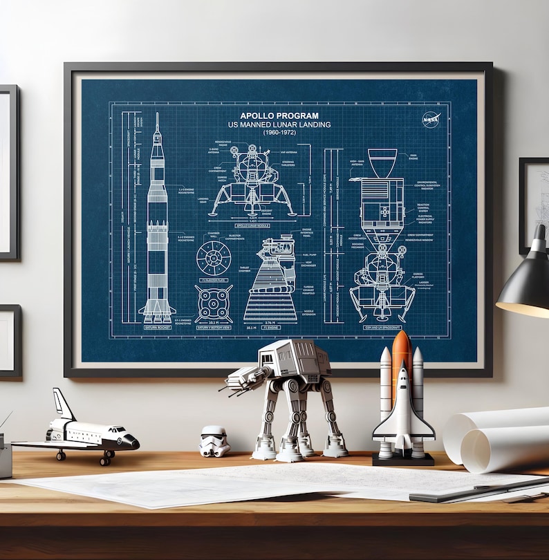 K&ouml;nnte beinhalten: Ein gerahmtes Poster im Blaupausenstil des Apollo-Programms US Manned Lunar Landing (1960-1972). Das Poster ist blau mit wei&szlig;en Strichzeichnungen der Rakete und der Mondlandef&auml;hre. Miniaturmodelle eines Raumschiffs, eines AT-AT-Walkers und eines Space Shuttles stehen auf dem Schreibtisch.