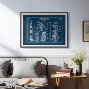 K&ouml;nnte beinhalten: Gerahmter Bauplan des Apollo-Programms US Manned Lunar Landing mit detaillierten Schemata der Saturn V-Rakete und der Mondlandef&auml;hre. Der Druck ist wei&szlig; auf dunkelblauem Hintergrund, in einem schwarzen Rahmen.