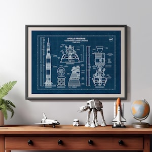 K&ouml;nnte beinhalten: Gerahmter Bauplan des Apollo-Programms, US Manned Lunar Landing (1960-1972). Der Druck befindet sich in einem schwarzen Rahmen und zeigt detaillierte Diagramme der Saturn V-Rakete und der Mondlandef&auml;hre. Ein Holztisch zeigt Figuren zum Thema Weltraum.