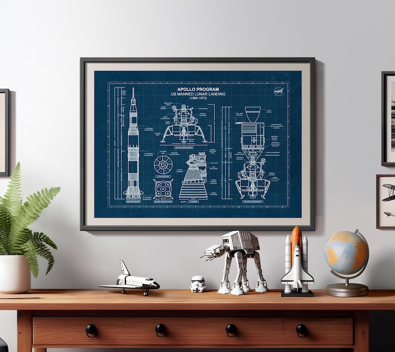 K&ouml;nnte beinhalten: Gerahmter Bauplan des Apollo-Programms, US Manned Lunar Landing (1960-1972). Der Druck befindet sich in einem schwarzen Rahmen und zeigt detaillierte Diagramme der Saturn V-Rakete und der Mondlandef&auml;hre. Ein Holztisch zeigt Figuren zum Thema Weltraum.