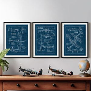 May include: Three blue framed prints of vintage airplane blueprints. The prints feature the Supermarine Spitfire, North American P-51 Mustang, and Hawker Sea Fury. The prints are displayed on a wall above a wooden table with two model airplanes and a globe.