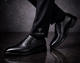 Peut inclure: Chaussures de ville en cuir noir avec lacets. Les chaussures sont portées avec un pantalon de costume noir. L'image a un fond sombre et réfléchissant. Le mot "FINETOO" est imprimé sur le pantalon.