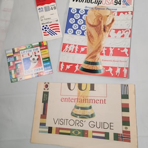 May include: A collection of four World Cup USA 94 memorabilia items. A ticket stub for a game in San Francisco, a program for the elimination round, a pamphlet with the text "Up for the Cup USA 1994" and a visitors guide with the text "World Cup entertainment Visitors' Guide".