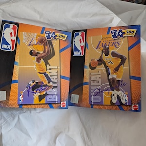 May include: Two NBA basketball card boxes featuring Kobe Bryant and Shaquille O'Neal in their Lakers uniforms. The boxes have the NBA logo and the text "7+" and "200". The background is a basketball court.