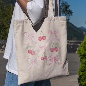 May include: A white tote bag with pink bows and cherries. The bag has a pink and white polka dot pattern on the bows.