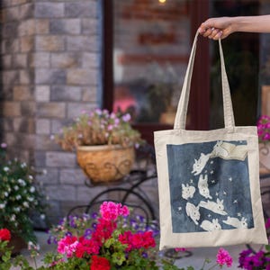May include: A beige tote bag with a blue background and white rabbits jumping in the air. The rabbits are surrounded by white stars. The bag has two long straps.