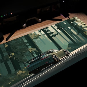 May include: A rectangular desk mat featuring a stylized illustration of a green sports car driving on a road through a forest. The car is angled, with the forest and road in the background. The mat is designed for use with a computer.