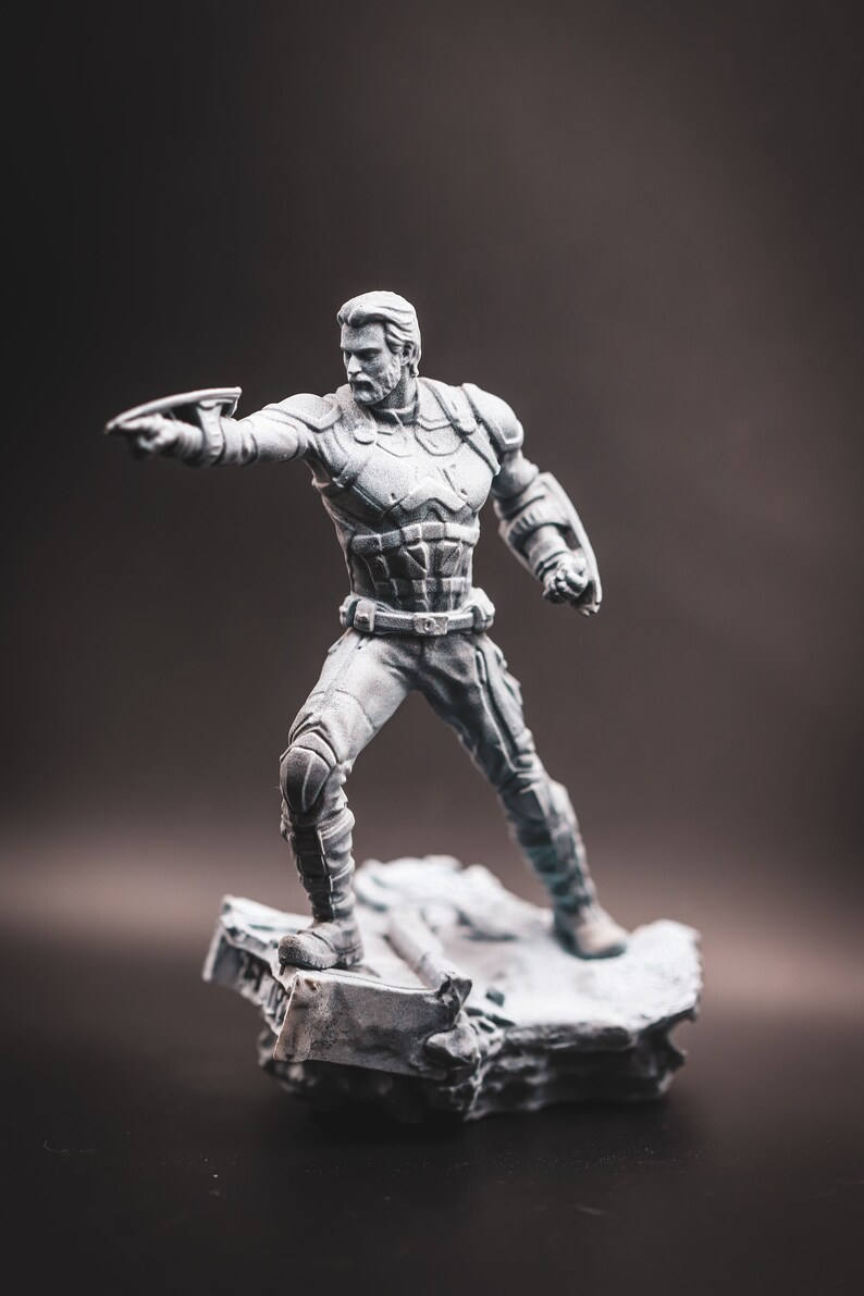 May include: A grey plastic figurine of a superhero standing on a grey plastic base. The superhero is wearing a suit with a belt and is holding a weapon in their right hand.