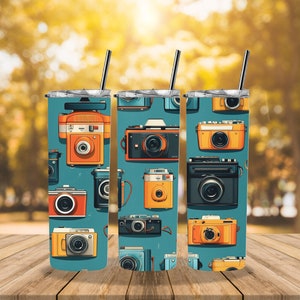 Puede incluir: Tres vasos de acero inoxidable con fondo azul y un patrón de cámaras vintage en varios colores. Los vasos tienen tapas y pajitas.