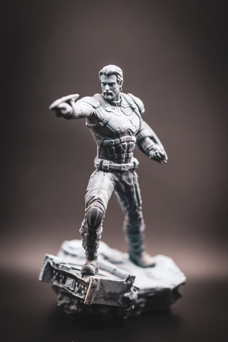 May include: A grey painted figurine of a superhero standing on a grey, rocky base. The superhero is wearing a detailed costume with a belt and is holding a weapon in their right hand.