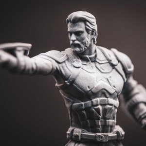 May include: A grey plastic figurine of a superhero with a beard, wearing a detailed costume with a belt and a textured chest piece. The figurine is holding a weapon in its right hand.