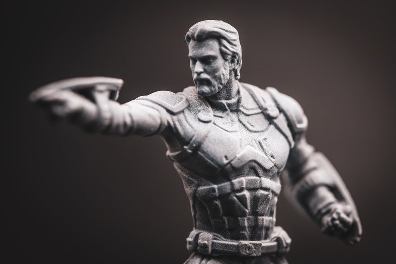 May include: A grey plastic figurine of a superhero with a beard, wearing a detailed costume with a belt and a textured chest piece. The figurine is holding a weapon in its right hand.