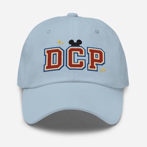 Peut inclure: Une casquette de baseball bleu clair avec les lettres "DCP" brodées en rouge et blanc avec une silhouette de Mickey Mouse noire au-dessus des lettres. Il y a deux étoiles dorées de chaque côté des lettres.