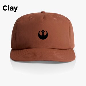 May include: A brown baseball cap with a black Rebel Alliance symbol on the front. The cap has a curved brim and a structured crown.