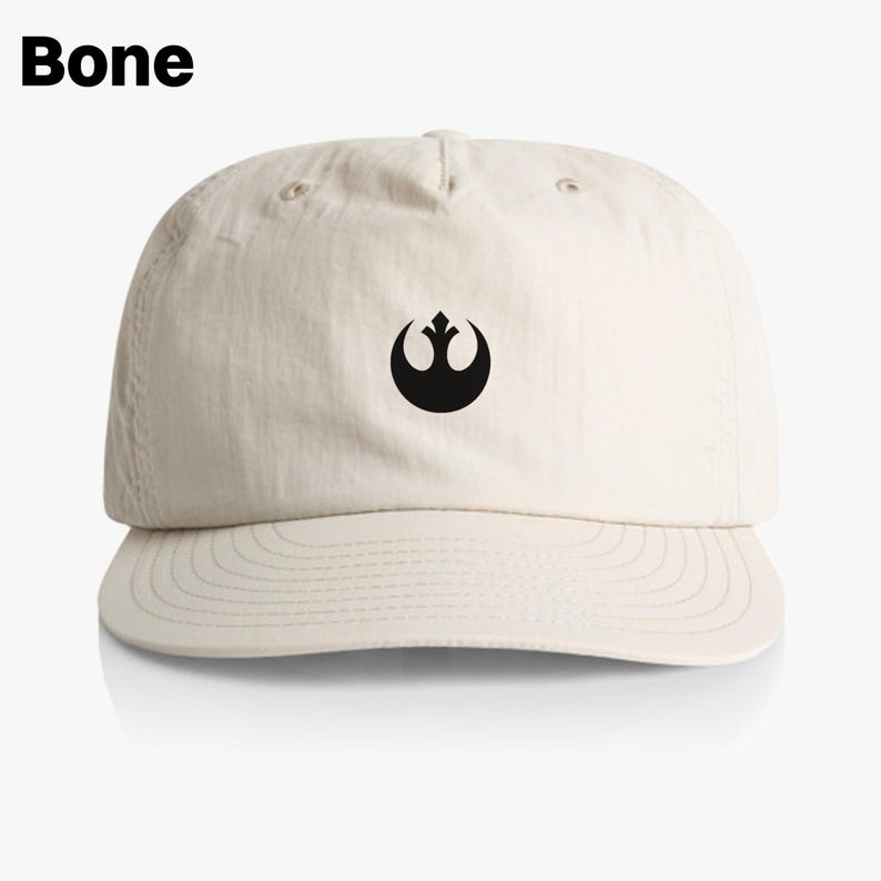 May include: A beige baseball cap with a black Rebel Alliance symbol on the front. The cap has a curved brim and a structured crown.
