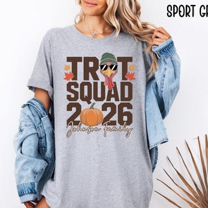 May include: A sport grey t-shirt featuring a graphic with the text TROT SQUAD 2026 and Johnson Family. The design includes a turkey wearing a green beanie and sunglasses, an orange pumpkin, and red and orange maple leaves on a grey background.