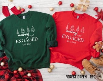 May include: Two sweatshirts, one forest green and one red, with the text "merry and ENGAGED EST. 2025" and Christmas tree graphics. The sweatshirts are surrounded by Christmas decorations, including ornaments and a gingerbread man.