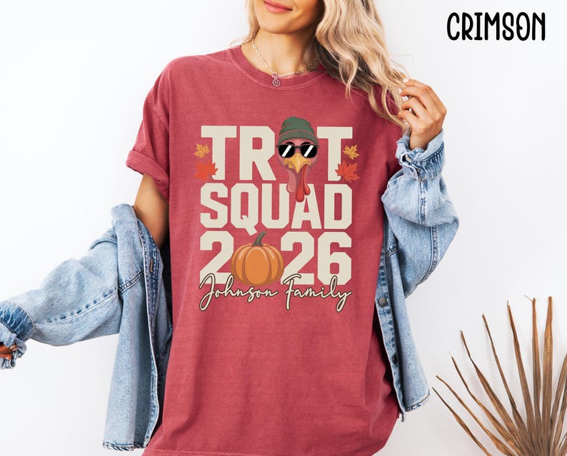 May include: A crimson short-sleeve t-shirt featuring a graphic of a turkey wearing a green beanie and sunglasses, with the text "TROT SQUAD 2026" and "Johnson Family" printed in cream, alongside a pumpkin and autumn leaves in orange and red.
