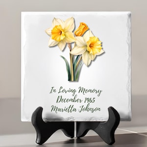 May include: White ceramic memorial plaque with a bouquet of yellow daffodils and the text "In Loving Memory December 1965 Marietta Johnson"