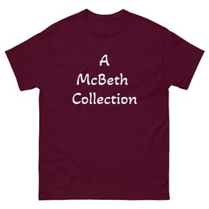 May include: A maroon t-shirt with the text "A McBeth Collection" in white, centered on the front. The shirt has a crew neck and short sleeves. The fabric appears to be a soft, comfortable material.