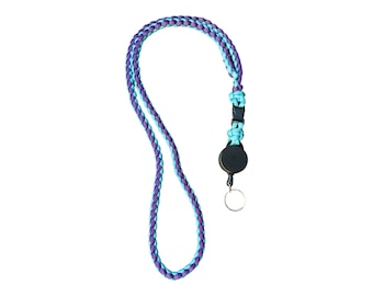 May include: A lanyard featuring a braided cord in alternating purple and light blue colors. The cord connects to a black plastic retractable badge reel and a circular metal split ring at the bottom, designed for holding identification or keys.