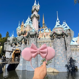 May include: Pink Minnie Mouse ears with a large bow in front of a castle decorated for the holidays.