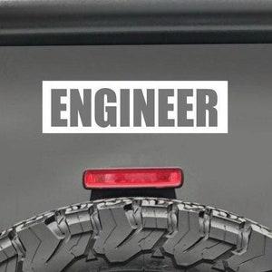 May include: A gray vehicle with a white sticker that says "ENGINEER" on the back. The vehicle has a spare tire on the back.