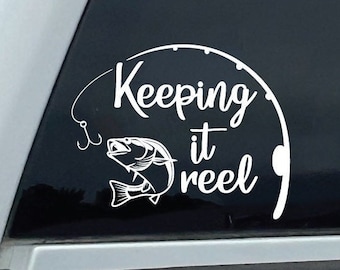 Könnte beinhalten: Weißer Vinyl-Aufkleber mit einem Design aus einer Angelrute und einem Fisch. Der Text lautet "Keeping it reel".